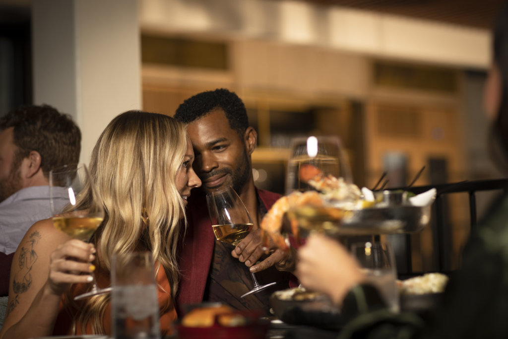 Couple Enjoying The Date Night Menu At Huntress, Man Leans Into Blonde Woman With Loving Expression