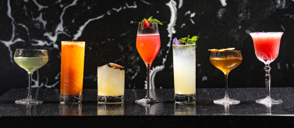 Various Cocktails Available At Huntress In A Single Line Against A Black Background